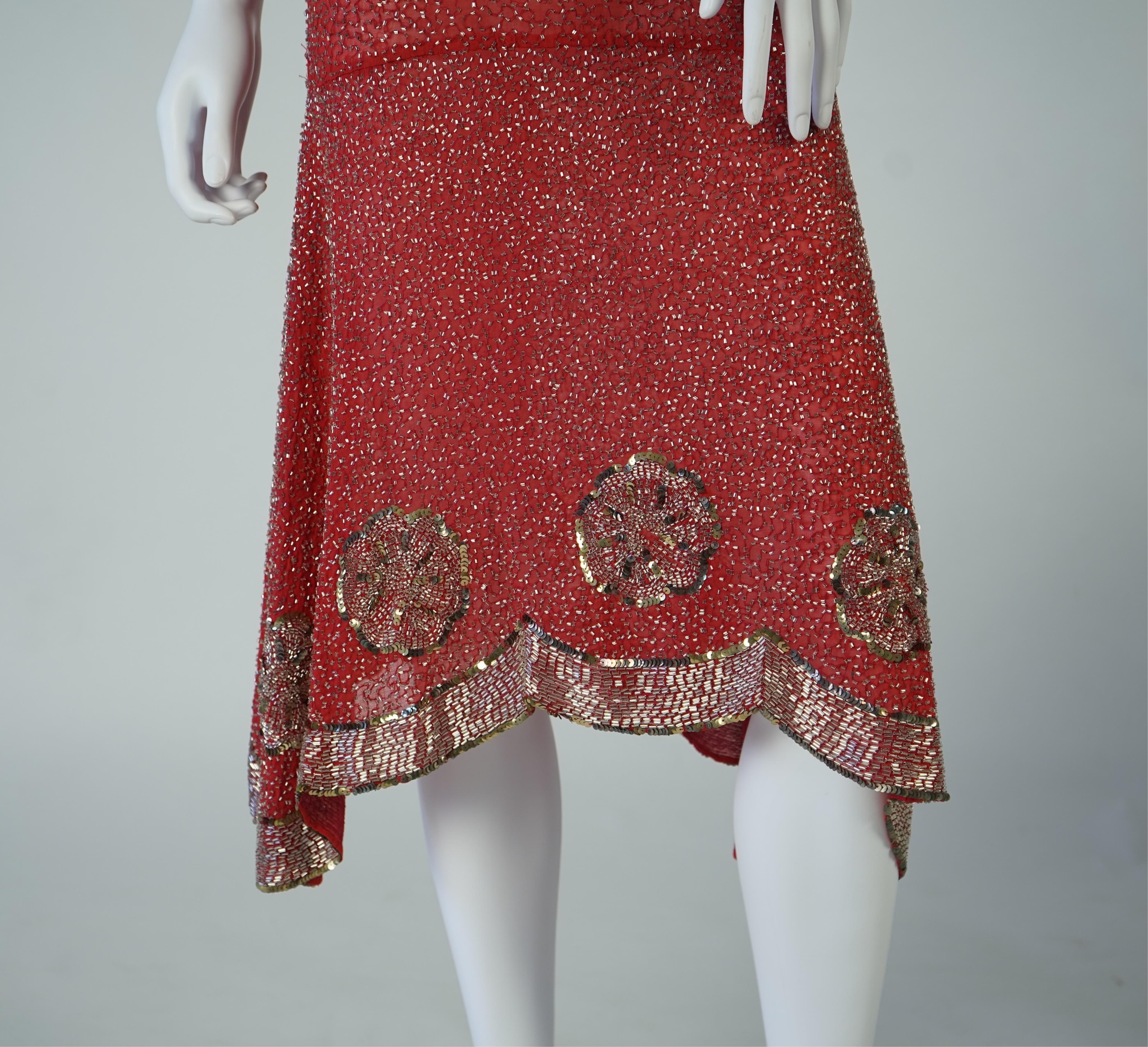 A 1920's red georgette beaded evening dress. Hand beaded and sequinned in white and gold, designed with a dropped waist, handkerchief points and wide beaded border with large stylistic floral motifs. Length 115cm. Condit